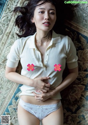 A woman in a white shirt and panties laying on a rug.