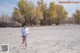 A woman running across a sandy field with trees in the background.