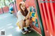 A young woman sitting on the ground in front of a playground.