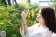 A woman in a white shirt is smelling a yellow flower.