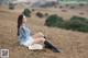 A woman sitting on a grassy hill with a cowboy hat.