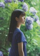 A woman in a blue dress standing in front of a bush of flowers.