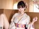 A woman in a pink kimono sitting on a bed.