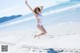 A woman in a white bathing suit jumping in the air on a beach.